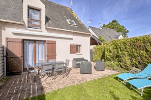 Een huis met een terras, straatmeubilair, een metselpad en een haag.
