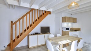 A modern kitchen with a wooden staircase, white cabinets, and a dining area with white chairs. - House with garden, 8 minutes Beach LA BAULE, residence with swimming pool (Guérande)