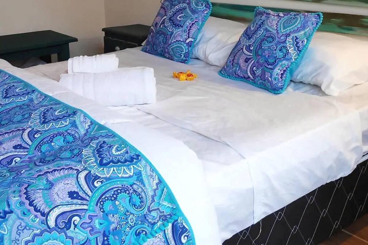 A neatly made bed with a blue patterned bedspread, two matching pillows, and a white blanket.