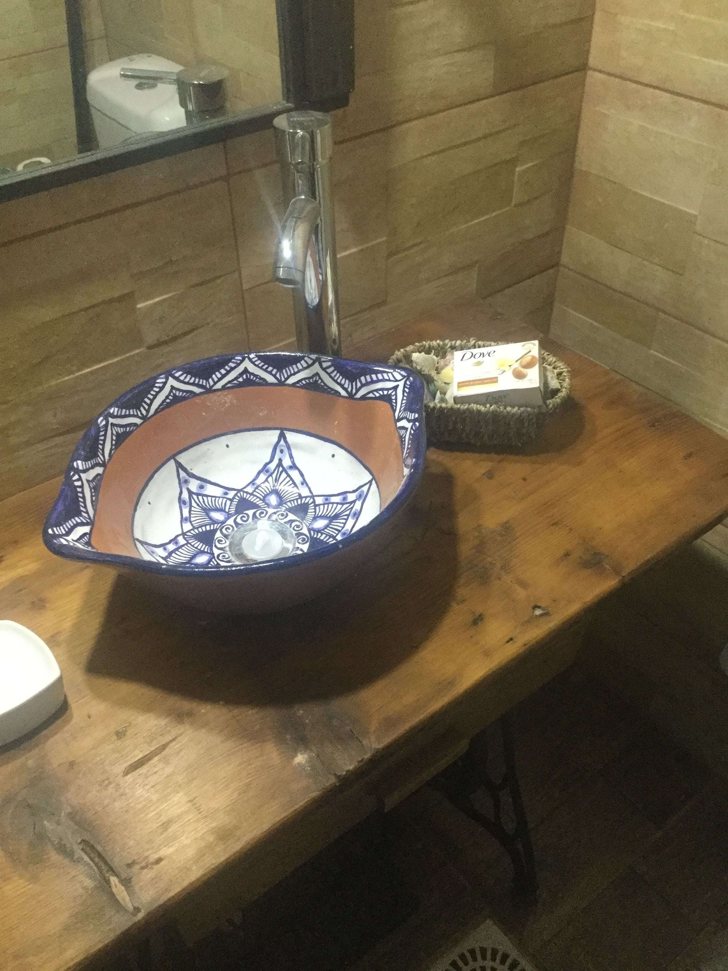 Une salle de bain avec un meuble-lavabo en bois, un évier en céramique orné d’un motif bleu et blanc, et un petit panier contenant une boîte de savon Dove.