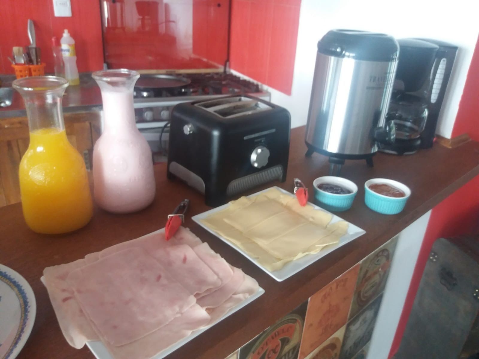 A kitchen counter with a toaster, a coffee maker, a kettle, and a plate of sliced meat.
