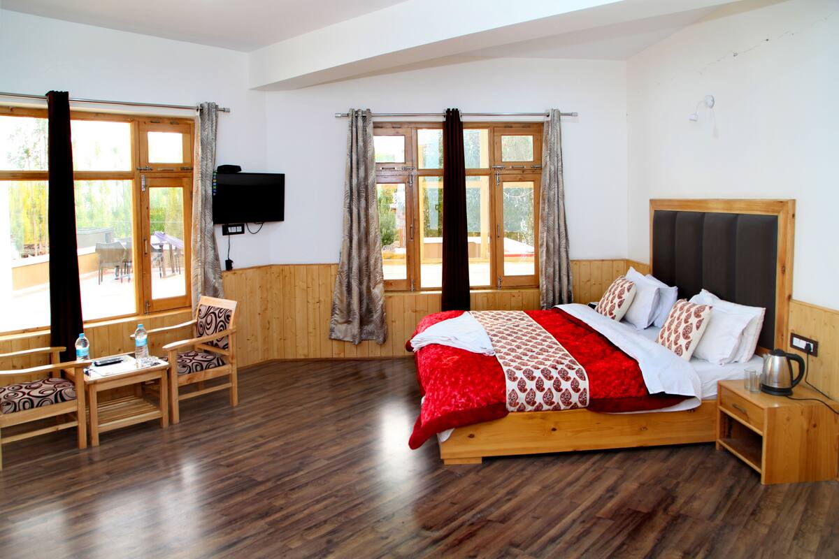 A bedroom with a wooden bed, a TV mounted on the wall, and large windows with curtains.