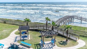 A beachside walkway with a wooden deck, palm trees, and a pool area.