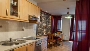Eine Küche mit Holzausstattung, einer Steinwand, einem Essbereich mit Tisch und Stühlen sowie einem roten Vorhang.