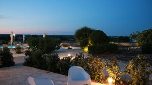 A poolside area with lounge chairs, a stone wall, and a view of the landscape.
