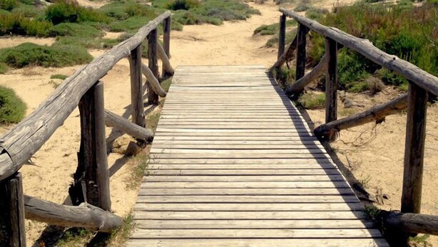 A wooden boardwalk leading to a beach with clear blue water.
