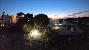 A nighttime outdoor area with a swimming pool, lounge chairs, and a building with an antenna.