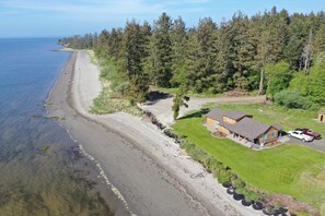 An aerial view of a coastal property with a beach, dense forest, and a house with a lawn and parked cars. - PEACEFUL BAYSIDE GETAWAY (Aberdeen)