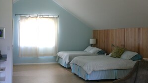 Ein Schlafzimmer mit zwei Betten, einem Fenster mit leichtem Vorhang und einem Holzkopfende.