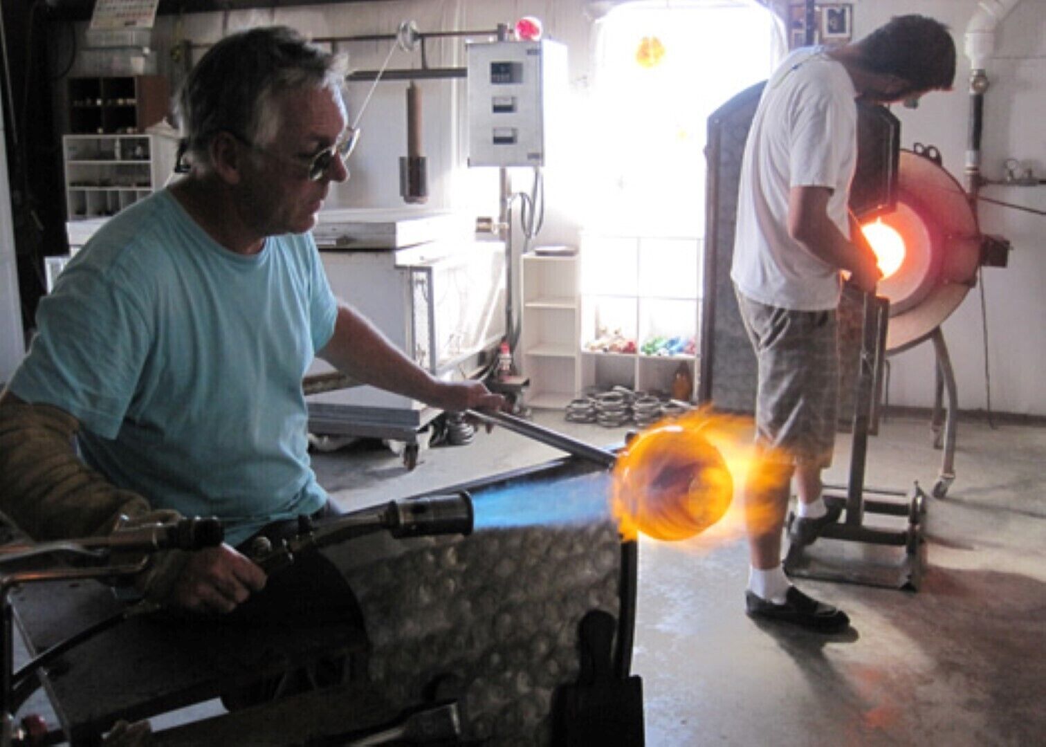 A workshop with two individuals working on a glassblowing project.