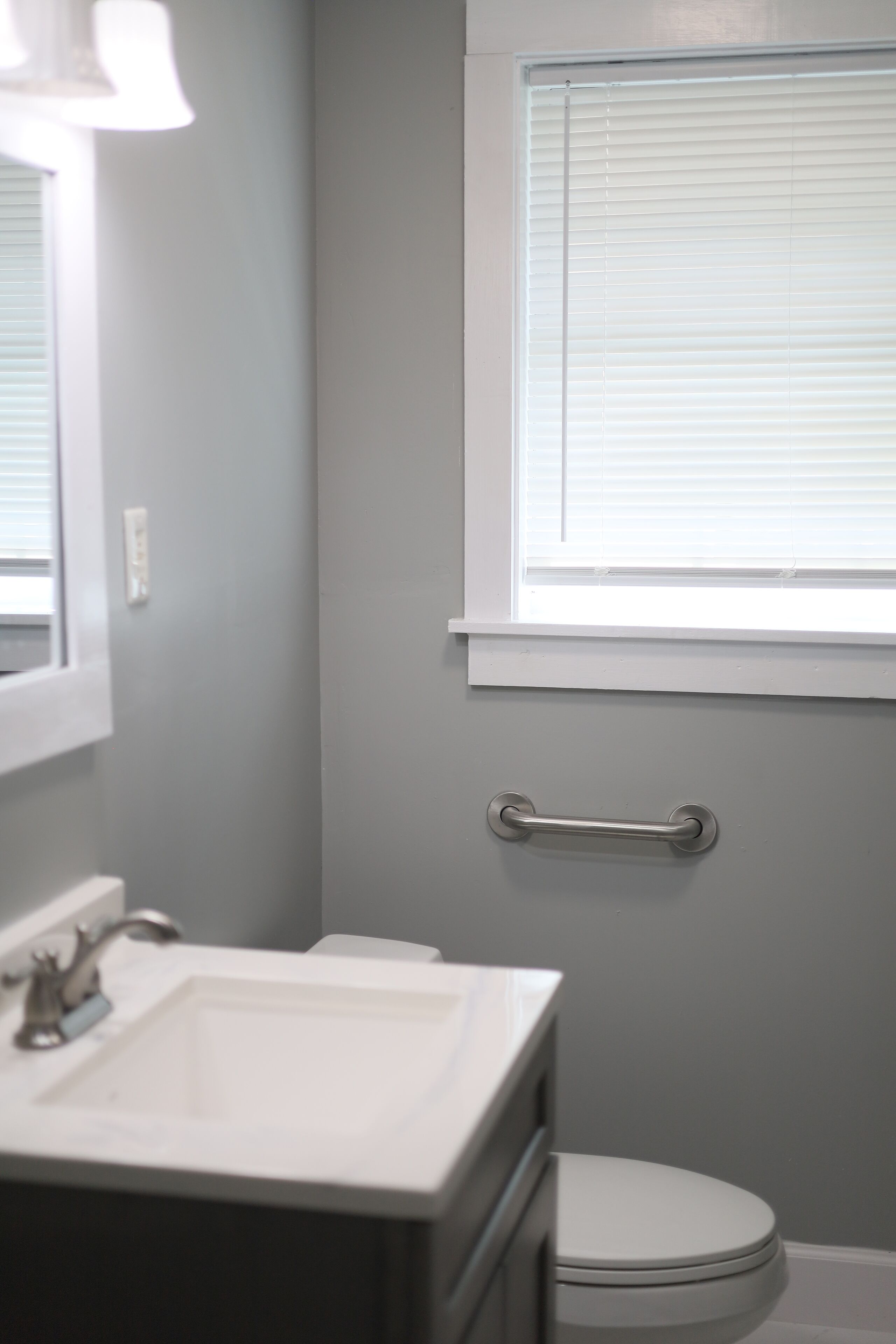 Ein Badezimmer mit Waschbecken, Toilette und einem Fenster mit Jalousien.