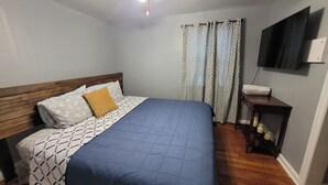 A bedroom with a bed, wooden headboard, patterned bedding, a blue bedspread, a nightstand with a lamp, and a TV mounted on the wall. - Spacious 2 Bedroom Home within 8 Minute walk to Downtown Augusta (Augusta)