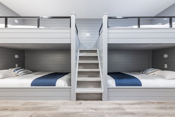 Habitación con literas, una escalera central, ropa de cama blanca y suelo de tono claro.