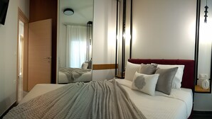 Quarto de hotel com uma cama, televisão na parede, mesa de cabeceira com abajur e janela com cortinas.