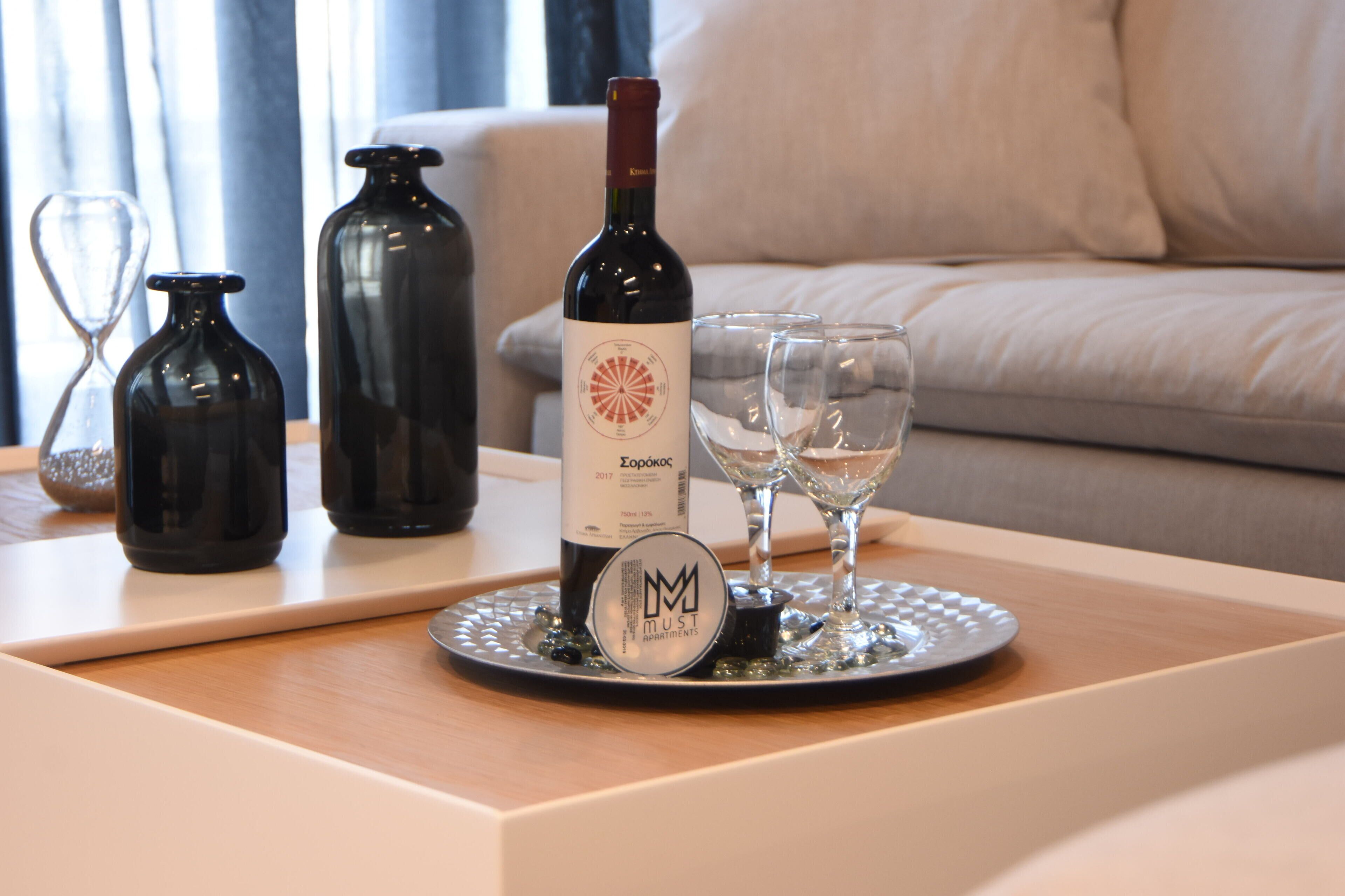 Una botella de vino, dos copas y botellas decorativas sobre una bandeja en una habitación con un sofá.