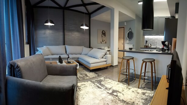 Uma sala de estar moderna com um sofá cinzento, uma mesa de centro e um espaço bar com banquetas.
