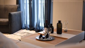 Uma bandeja bem organizada com garrafas de vinho, copos e um ampulheta sobre uma mesa de madeira em um quarto com sofá e cortinas.