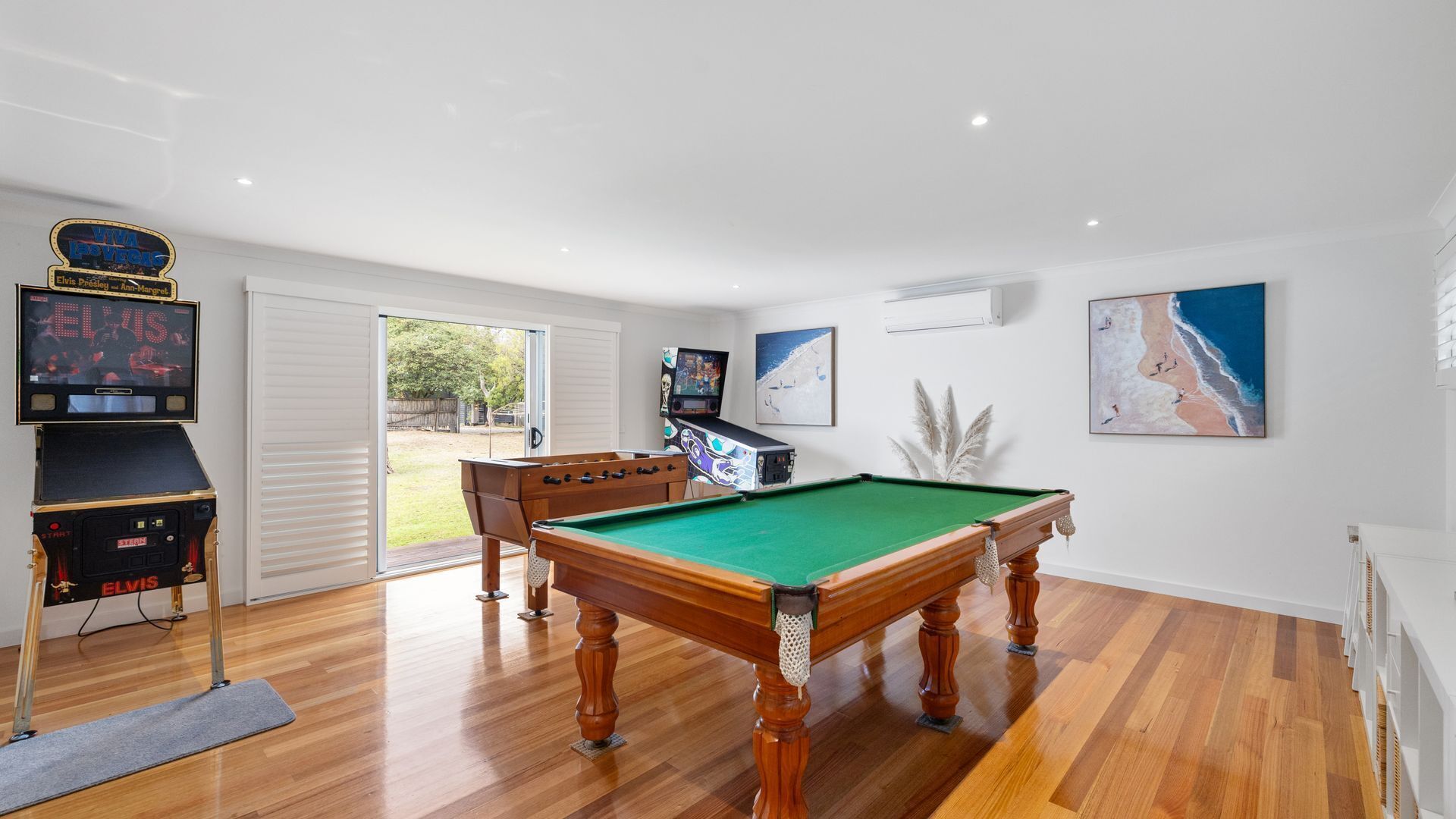 A room with a pool table, a foosball table, a television, and a large window.