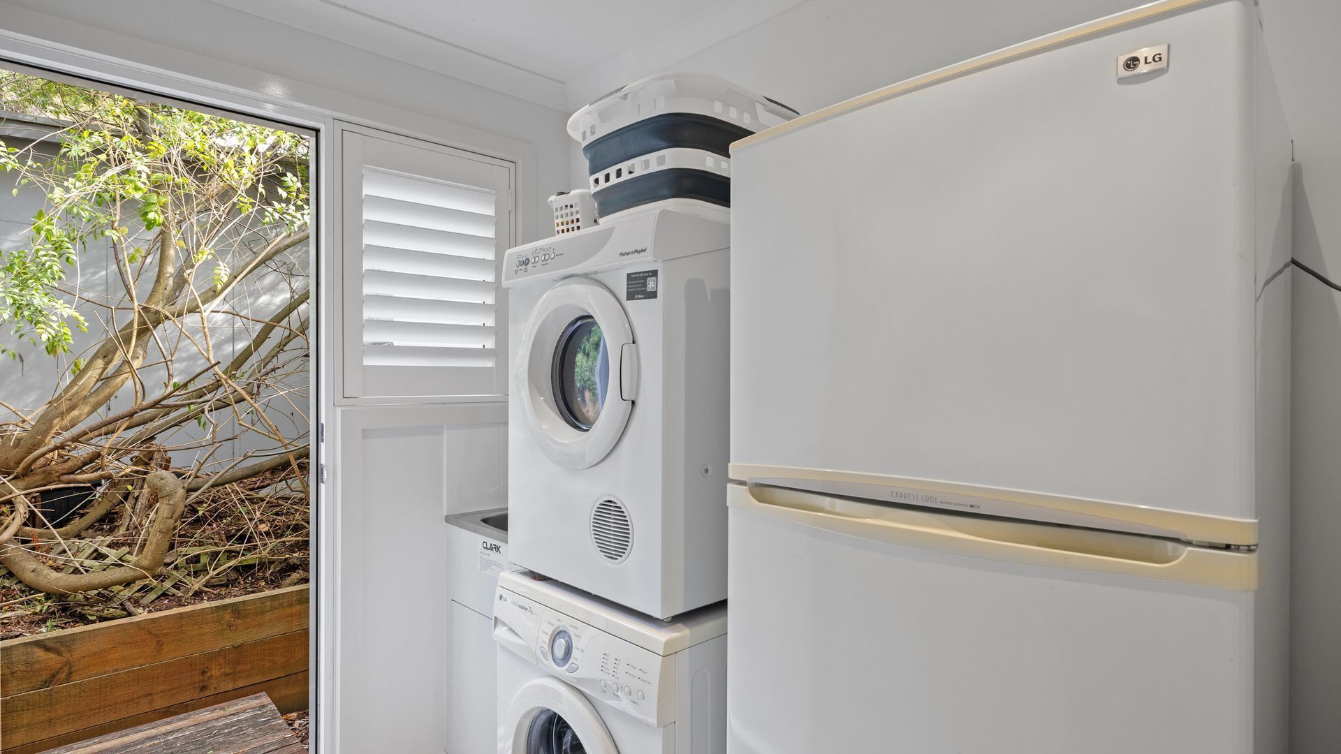 A compact laundry area with a front-loading washer, a stacked dryer, and a white refrigerator.
