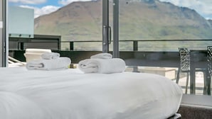 Ein Hotelzimmer mit einem Bett, zwei zusammengerollten Handtüchern, einem Fenster mit Bergblick und einem Balkon mit Stühlen.