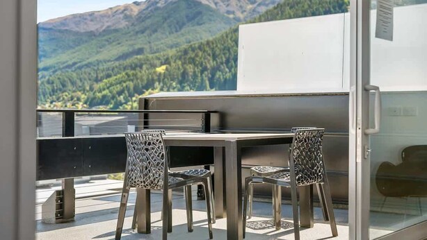 Ein Balkon mit Tisch und Stühlen mit Blick auf eine gebirgige Landschaft.