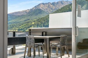 A balcony with a table and chairs, overlooking a mountainous landscape.