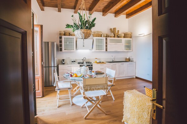Cocina moderna con armarios blancos, una planta colgante y un comedor con mesa preparada para cuatro.