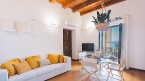 A modern living room with a white sofa, wooden flooring, and a dining area with a glass table and chairs. - DuoMo SeaView PlatinHome-Luxurious, renovated, air-conditioned-Sea View-WiFi (Siracusa)