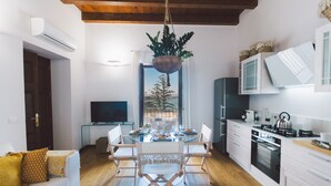 A modern kitchen with white cabinets, a dining table with chairs, a hanging plant, and a view of the outdoors. - DuoMo SeaView PlatinHome-Luxurious, renovated, air-conditioned-Sea View-WiFi (Siracusa)