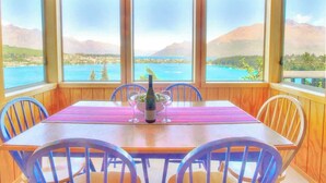 Un comedor con una mesa preparada para cuatro personas, amplios ventanales que ofrecen vistas a un lago y montañas, y una botella de champán sobre la mesa.