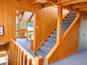 A wooden interior with a staircase, a bed, and a view of the outdoors.