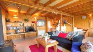 Una sala de estar acogedora con vigas de madera, una chimenea, un sofá y un televisor.