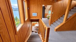 A wooden interior with a staircase leading to a balcony overlooking a lake.