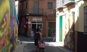 Une rue étroite avec un bâtiment portant l’inscription « CASA ESTEBAN MAS BARATO » et une fresque murale sur le côté gauche.