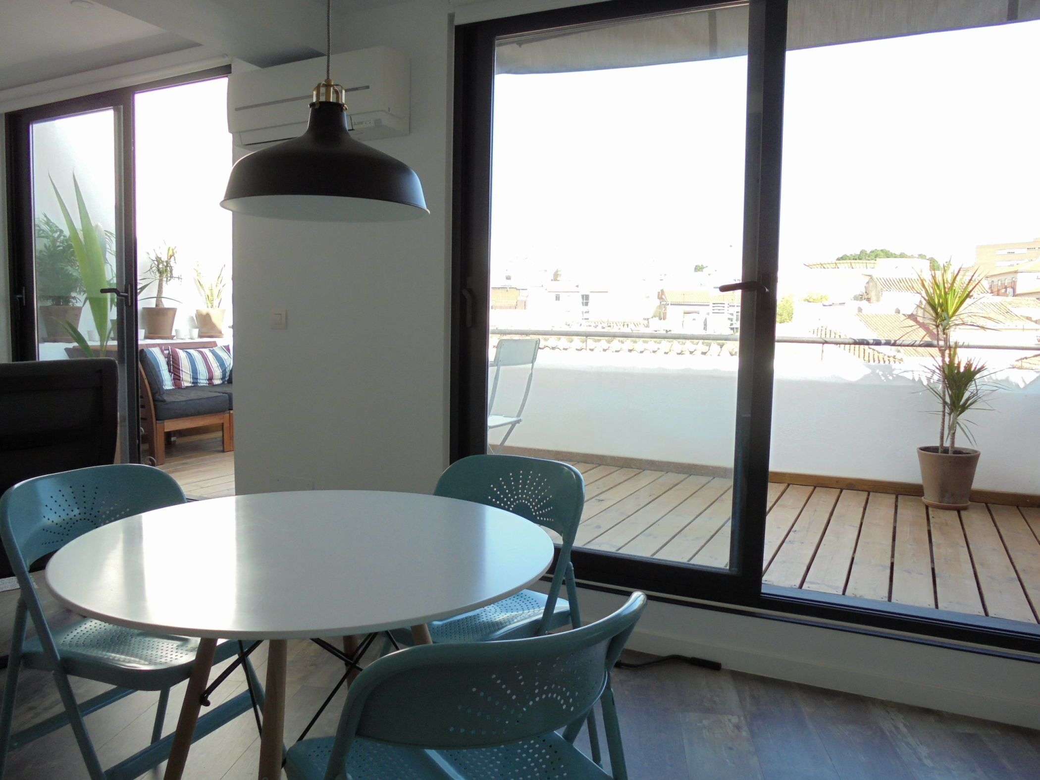 A modern room with a round table and chairs, large windows, and a balcony with potted plants.