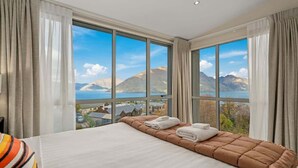 Une chambre d’hôtel avec un grand lit, une vue sur les montagnes et un lac, et une fenêtre avec des rideaux.