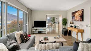 Un salon moderne doté d’un téléviseur à écran plat, de canapés gris, d’une table basse et de grandes fenêtres offrant une vue sur les montagnes.