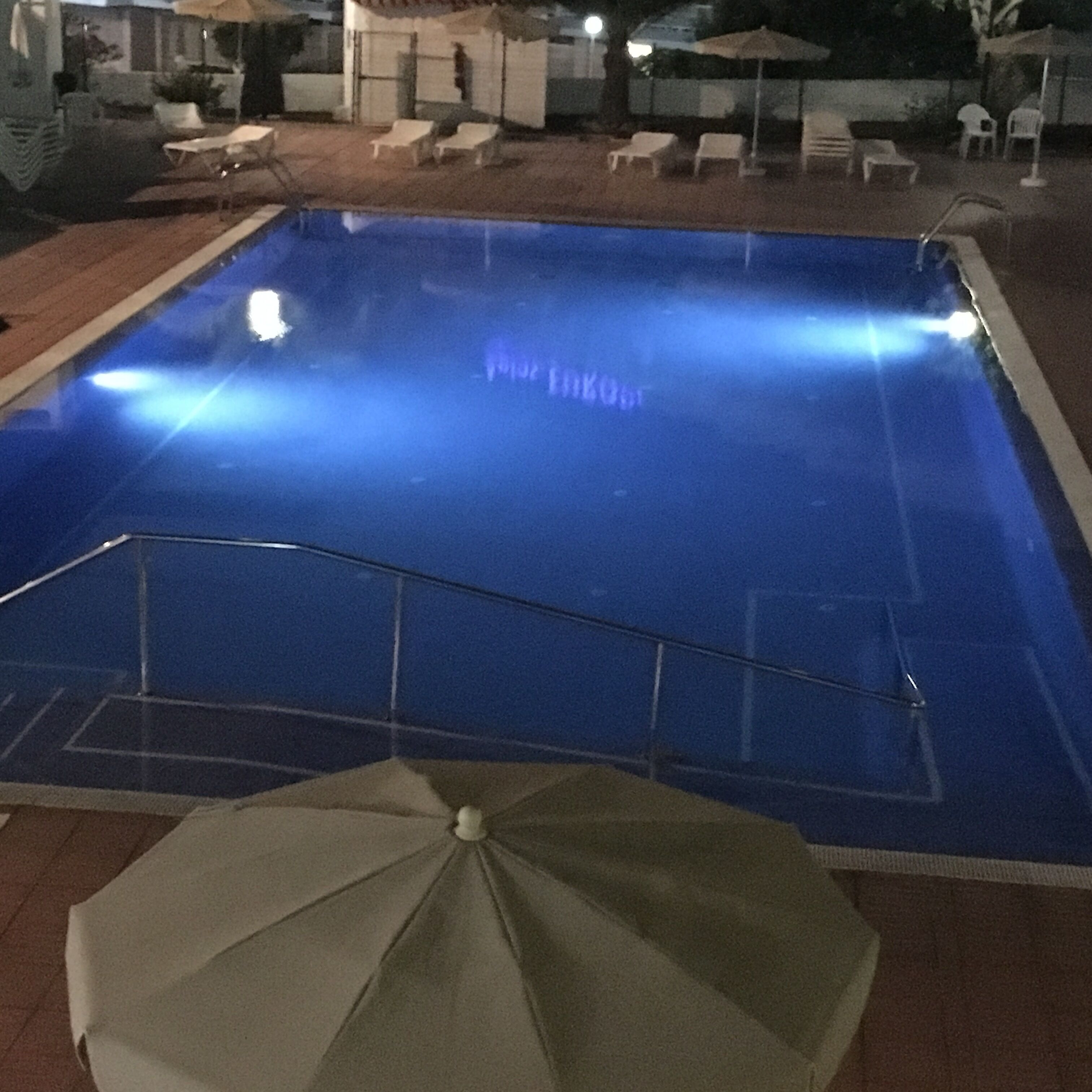 En swimmingpool med en metallstege och ett enda parasoll.