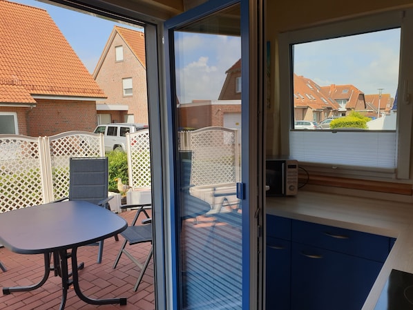 A room with a sliding glass door leading to a patio area with a table and chairs, a white fence, and a view of neighboring houses.