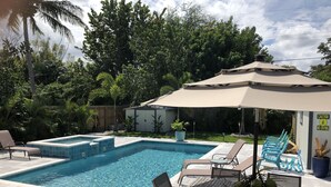Une piscine rectangulaire avec des marches carrelées, entourée de chaises longues et d’une table dotée d’un parasol.