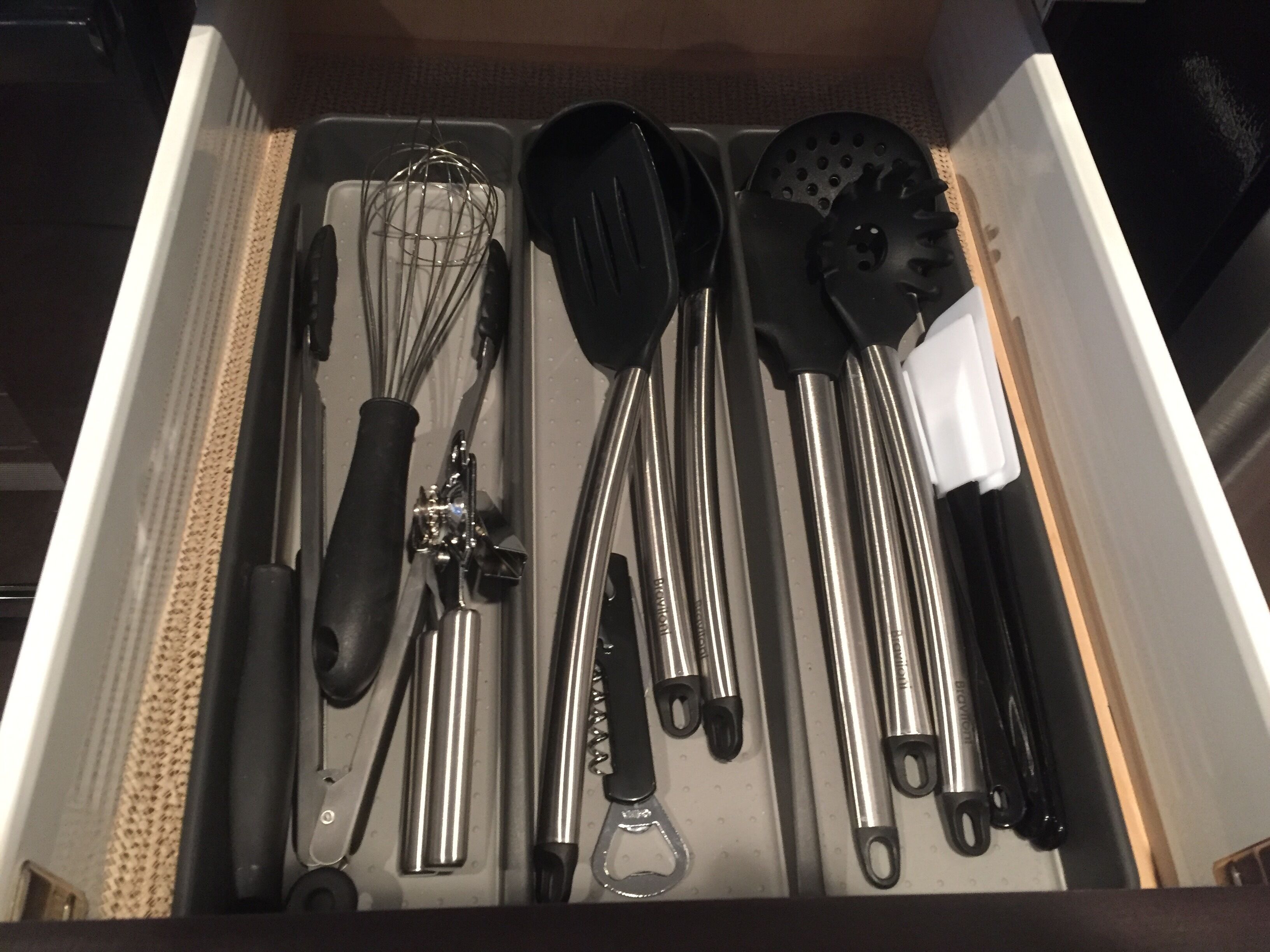 A drawer containing various kitchen utensils including a whisk, spatula, and tongs.
