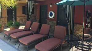 Outdoor seating with cushioned chairs and a table, a potted plant, and a door with a stone wall.