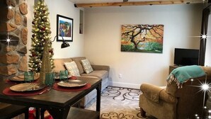 A cozy living room with a stone wall, a Christmas tree, a painting, and a dining area with a table set for a meal.