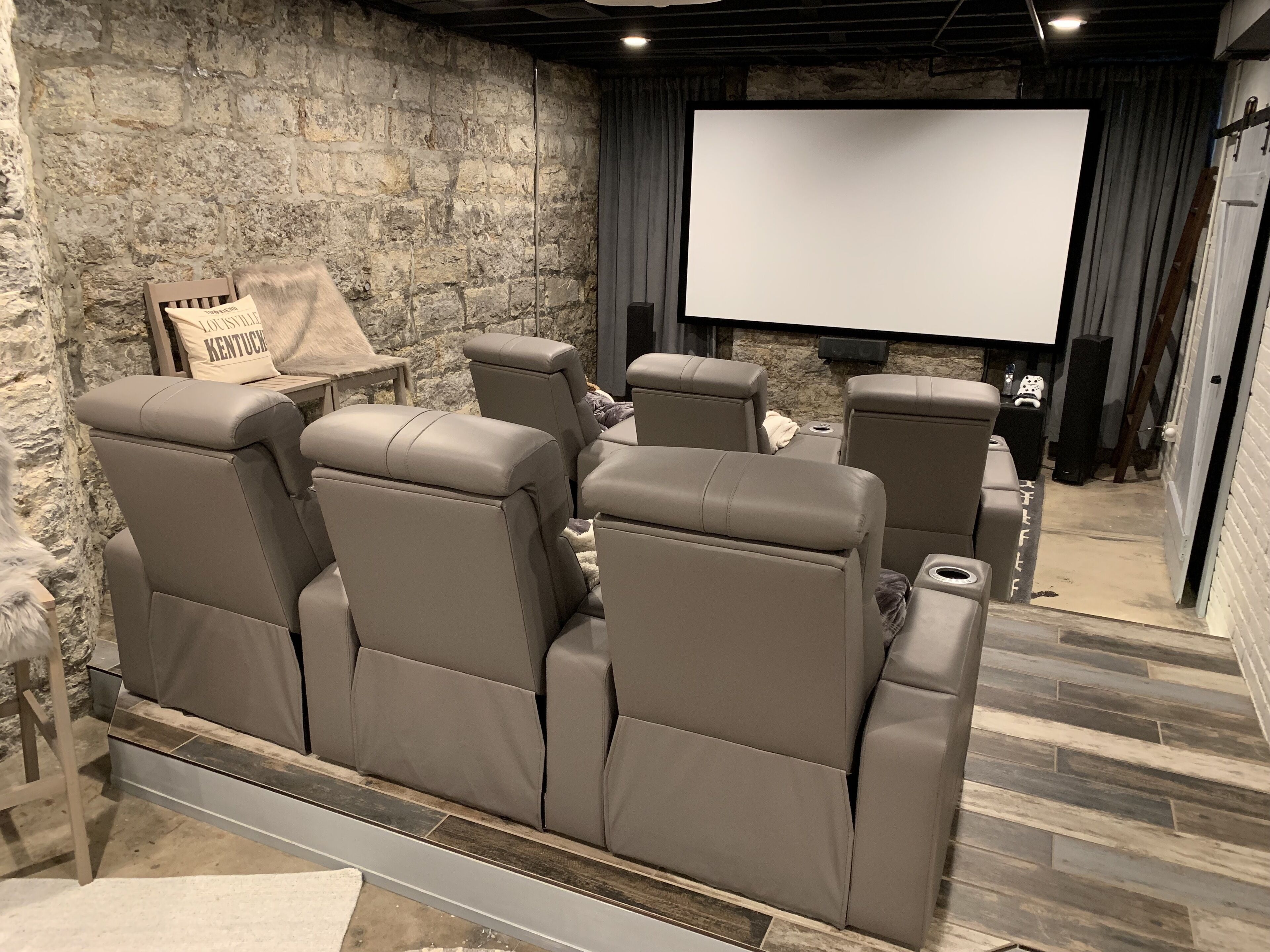 A home theater with six leather recliner seats, a stone wall, and a large screen.