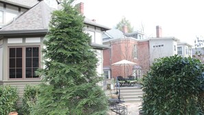 Una zona residencial con una casa que tiene un patio de piedra, mobiliario exterior y un gran árbol de hoja perenne.