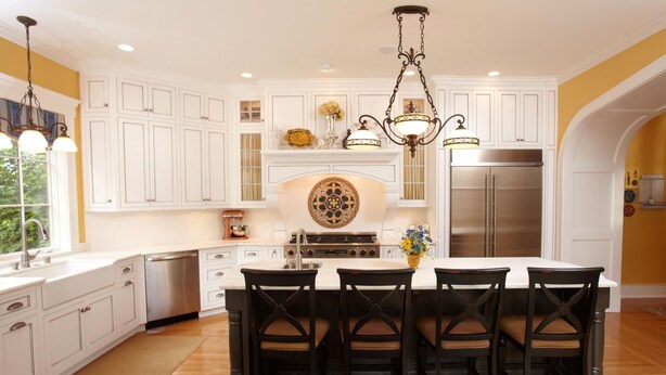 Cocina con armarios blancos, una isla central con cuatro sillas, un refrigerador de acero inoxidable y un salpicadero decorativo.