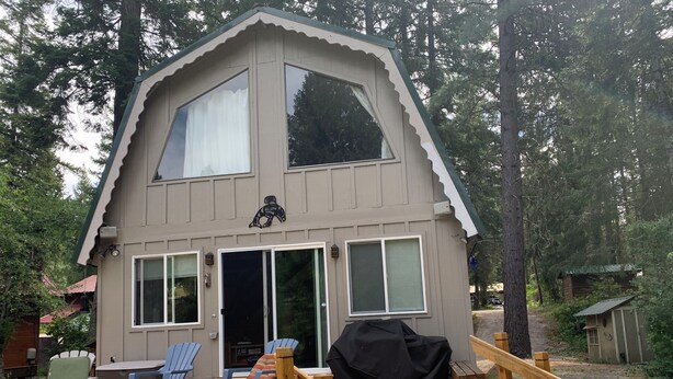 A cabin with a wooden deck, a covered outdoor seating area, and a staircase leading to the entrance. - River Front Cabin in Plain, close to Lake Wenatchee

Short term rental #000168 (Leavenworth)