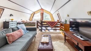 A cozy living room with a sofa, a coffee table, a TV, and a staircase leading to a loft area with a large window. - River Front Cabin in Plain, close to Lake Wenatchee

Short term rental #000168 (Leavenworth)