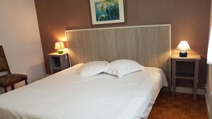 Un lit bien fait, avec du linge de maison blanc, dans une pièce dont les murs sont recouverts de lambris en bois et où un tableau est accroché au-dessus du lit.
