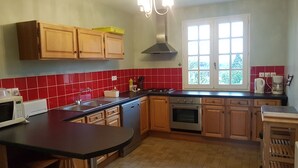 Une cuisine avec des meubles en bois, un plan de travail noir, une cuisinière et une fenêtre donnant sur des arbres.